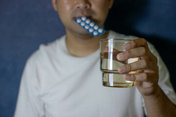A man's hand holds a pill pack and holds it in his mouth.
Another hand holds a glass of water. To...