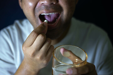 Male hand holding white pills
round and glass of water to take medicine Treat sickness Treat pain...