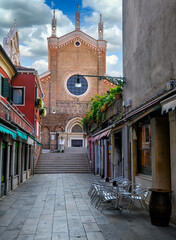 Old street with church and tables of restaurant in Venice, Italy. Architecture and landmark of Venice. Cozy cityscape of Venice.
