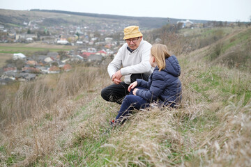 Naklejka na ściany i meble Active senior and his grandson sitting on top of the hill and contemplating the landscape. Happy family active outdoor. Active activity in old age