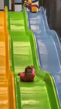 Vertical shot of two young girls playing on a colorful playground slide