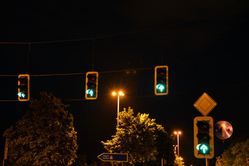 Several traffic lights hang over a night city road against a background of dark sky and trees