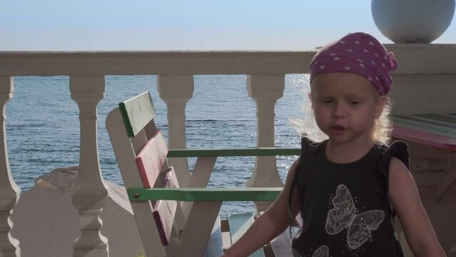 Little girl on the sea coast background expresses doubt, shrugging shoulders.
