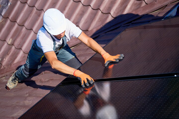 Worker building solar panel system on rooftop of house. Man engineer in helmet and gloves...
