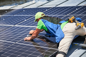 Worker building photovoltaic solar panel system on rooftop of house. Man engineer installing solar...