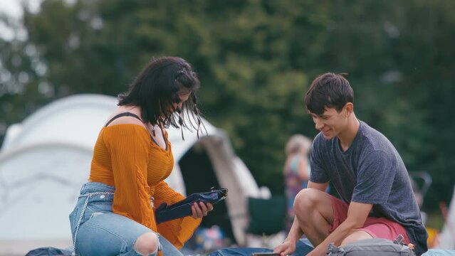 Young couple unpacking and setting up tent for camping at outdoor summer music festival - shot in slow motion
