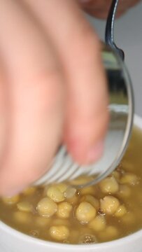 A man pours canned chickpeas from a tin can into deep white ceramic bowl, vertical close-up video.