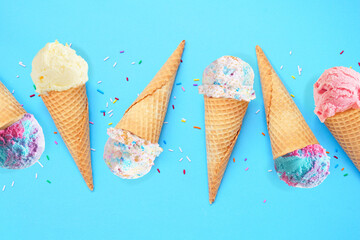 Summer ice cream cone flat lay over a blue background. Variety of pastel colored flavors.