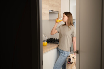 Young woman in the kitchen drinking juice with her dog. A happy girl strokes her dog before breakfast