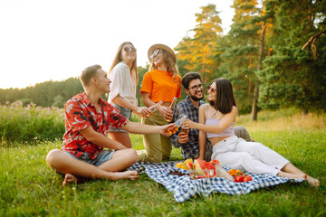 Group of young people having fun while drinking beer at picnic party. Friends enjoy sunny day. Vacation, weekend, friendship or holliday concept.