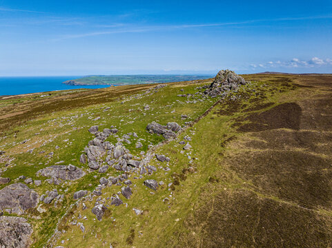 Aerial shot of exposed rocky outcrops surrounded by moorland and farmland with coastline in the distance. Pembrokeshire, Wales