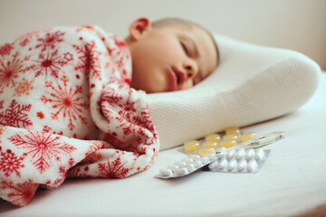 Sick little boy sleeping in white bed with a thermometer and antipyretic tablets on a orthopedic pillow
- 790318159