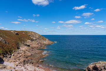 À Pléhérel-plage, les falaises rocheuses surplombent des eaux turquoises, sous un ciel d'un bleu éclatant, offrant un paysage à couper le souffle.