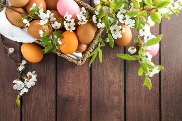 A beautiful bouquet of flowers and colorful Easter eggs displayed in a basket on a rustic wooden...