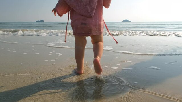 Cute baby girl walking on the beach shoreline with mother in the morning, slow motion