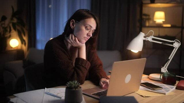 Tired freelancer having distance remote work typing browsing scrolling products in internet online store on laptop computer while sitting at desk workplace at late night at home