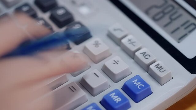 A calculator with a blue button that says MC. A person is using the calculator. The calculator has a black and white keypad