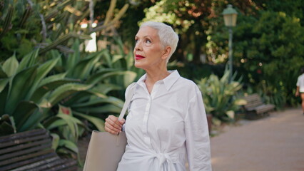 Mature woman strolling garden admiring greenery. Relaxed grey hair lady walking