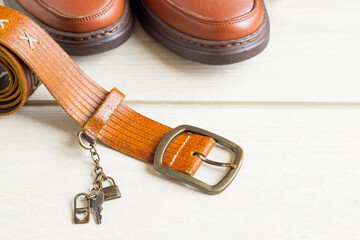 Brown leather belt with men's shoes on wooden surface