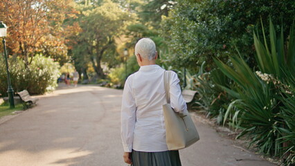 Relaxed senior walking park admiring nature back view. Calm grey hair woman