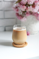 Coffee with milk in a transparent glass without an ear in the sun's rays, a bouquet with Japanese cherry blossoms stands on the back
