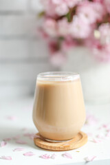 Coffee with milk in a transparent glass without an ear in the sun's rays, a bouquet with Japanese cherry blossoms stands on the back