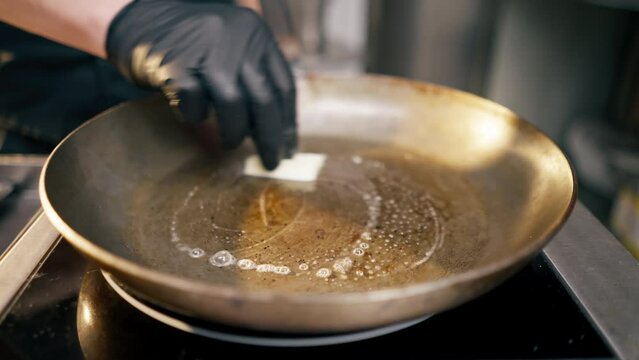 close-up in the kitchen a hand in a black glove butter a bun on hot frying pan