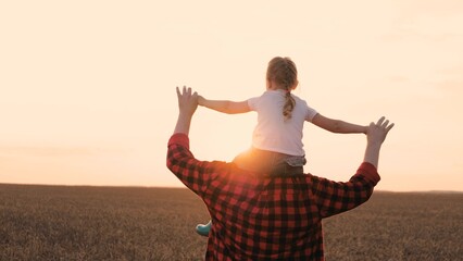 Playful family father and daughter walking at sunset sky dry wheat field slow motion. Happy male parent and little girl kid child flying on shoulders enjoy freedom childhood outdoor leisure closeup - obrazy, fototapety, plakaty