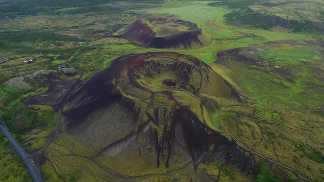 Epic Aerial Grabrok Crater Iceland Drone Back Through Clouds to Wide Landscape. Ancient Volcano Red Rock and Lush Green Grass and Mountains. 4K High Quality Color Corrected.