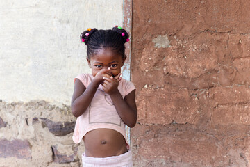 african girl with braids and beads pulling funny faces in front of a wall in the township