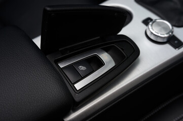 A car's dashboard has a black leather cover with a silver button. The button is labeled 