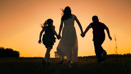 silhouette mother runs into sunset holding her son daughter hand, happy family running, boy girl,...