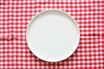 an empty plate on a red checkered tablecloth, top view. flat layout. kitchen mockup.