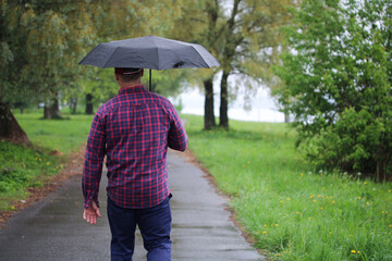 man in a plaid shirt walks under an umbrella down an alley in the rain.