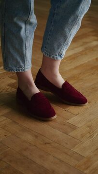 Person wearing burgundy slip-on shoes with rolled-up blue jeans on a herringbone parquet floor. Casual footwear style and comfortable fashion concept for design and advertising.
