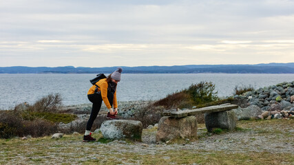 Naklejka na ściany i meble A woman secures her shoe on a coastal trail, preparing for an active walk along the sea. Concept: adventure, readiness, outdoor activity