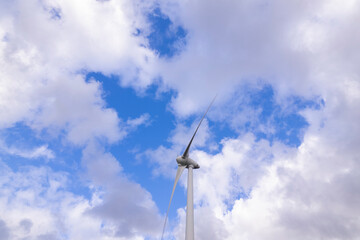 White cumulus clouds behind a electricity generating three bladed wind turbine seen from below
