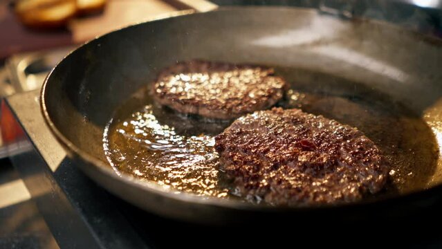 close-up in the kitchen of the establishment frying two beef cutlets in frying pan