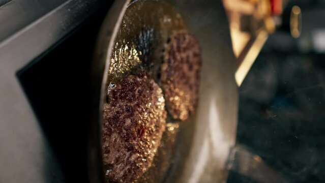 vertical video close-up in the kitchen of the establishment frying two beef cutlets in frying pan