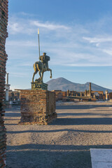 View of a bronze statue at the ruins of the Forum during golden hour at sunset with volcano mount Vesuvius in background, Pompeii, Campania, Italy