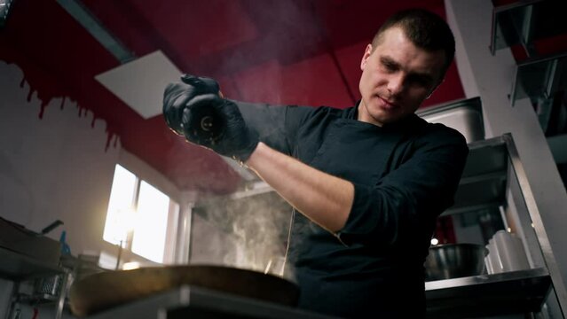 Chef in a professional kitchen bottom view salts the contents in a frying pan