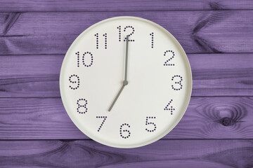 Round white wall clock at 7 o'clock on purple wood background. concept of daily regime, wake up...