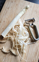 White Asparagus on wooden cutting kitchen board next to peeeller and asparagus peelings. How to...