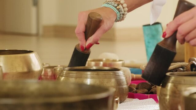 Mentor creates soothing sounds of singing bowls with mallets. Skilled woman enables to explore innermost thoughts and emotions with ease