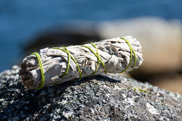 An image of a white sage smudge stick with bright green thread resting on a lichen covered rock. 