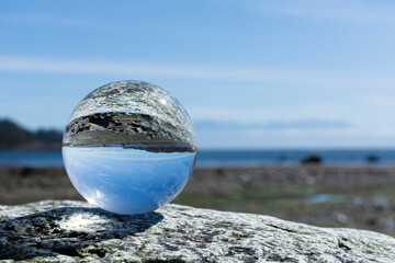 An image of a photographic lens ball resting on a rock and reflecting the image of the rocky coastline and Pacific Ocean.