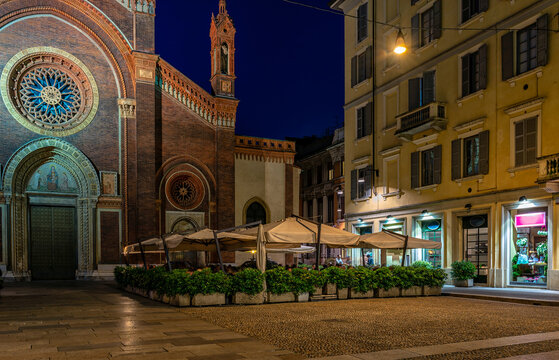 Old square with restaurant tables in front of the church Santa Maria del Carmine in Milan, Italy. Night cityscape of Milan. Architecture and landmarks of Milan.