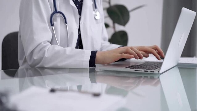 Doctor woman is working with laptop computer at the glass table in clinic. Physician is typing medical information or giving advices online. Medicine and pharmacy