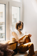 Serene brunette woman enjoys coffee by window at home.