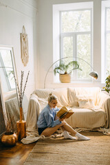 Young happy woman sitting on the floor at home in the morning with a book and coffee.